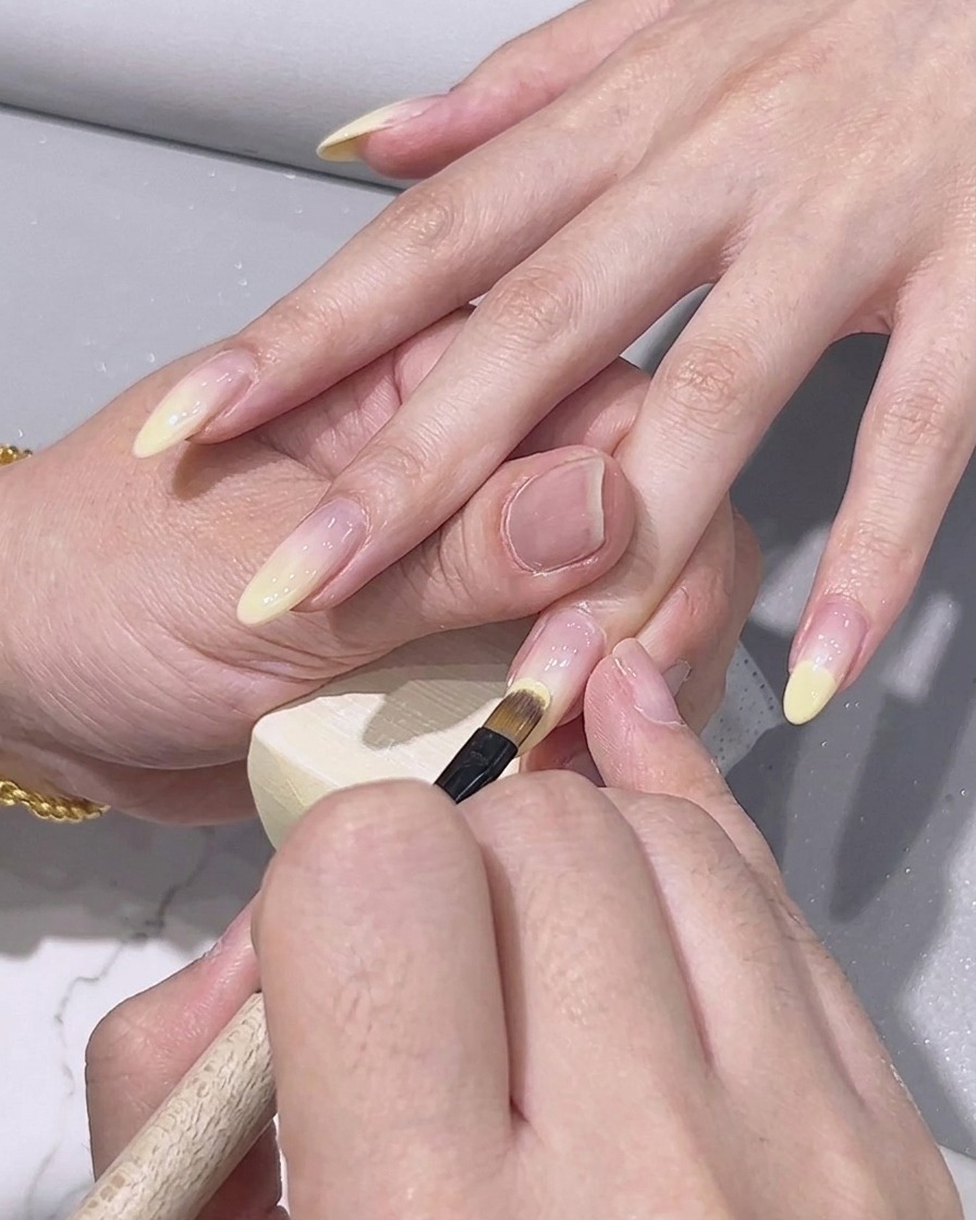 Ein feiner Detailpinsel trägt helles zitronengelbes Gel-Polish auf die Nagelspitze auf.