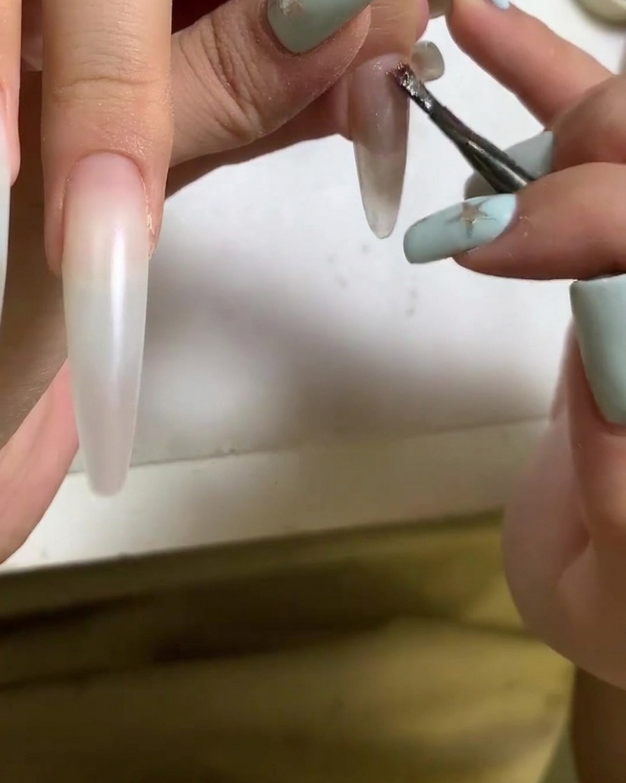 Ein Pinsel trägt Cat-Eye-Gel-Polish auf die Oberfläche eines Acrylnagels auf.