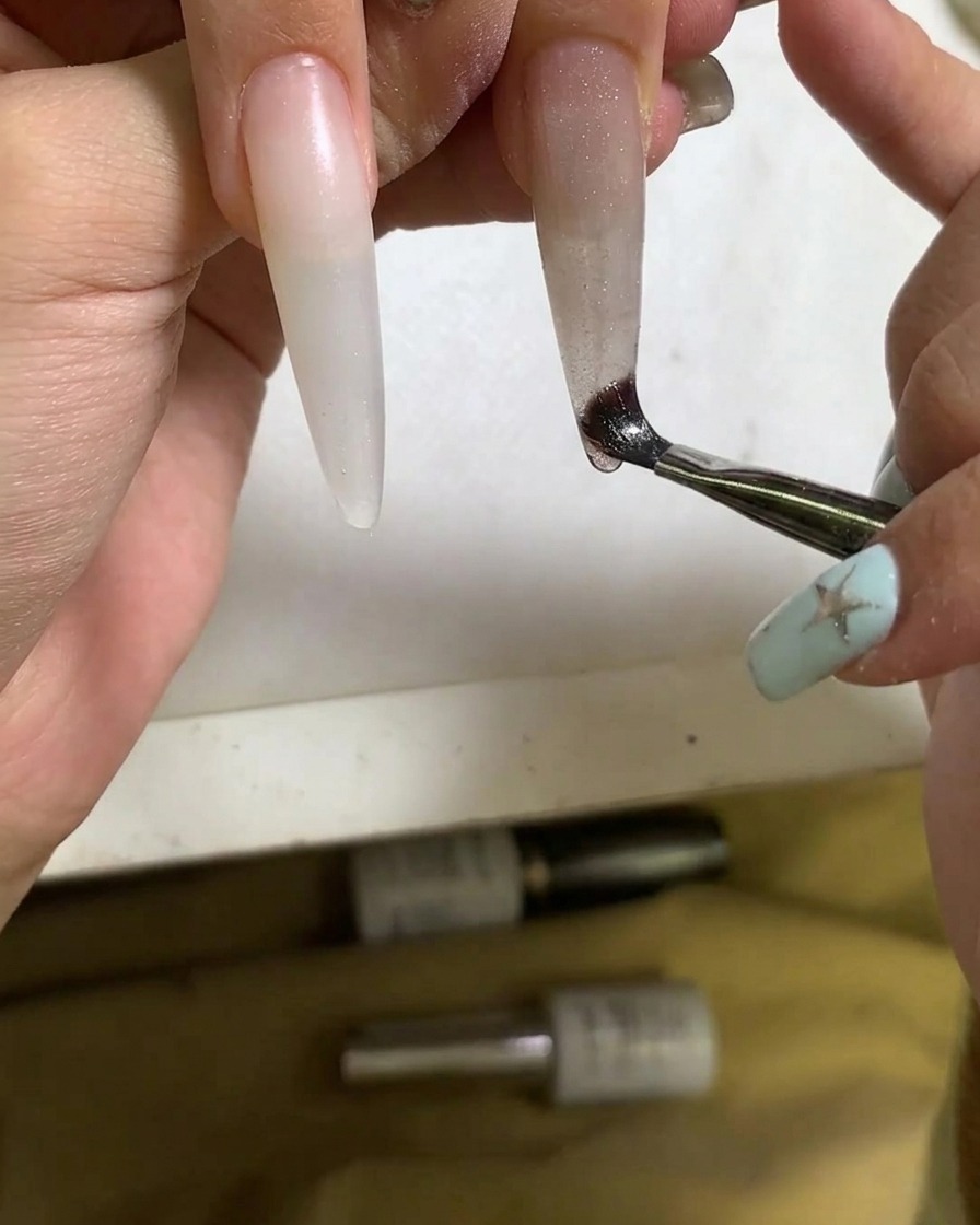 Nahaufnahme eines Pinsels, der Cat-Eye-Gel-Polish auf den Nagel aufträgt.