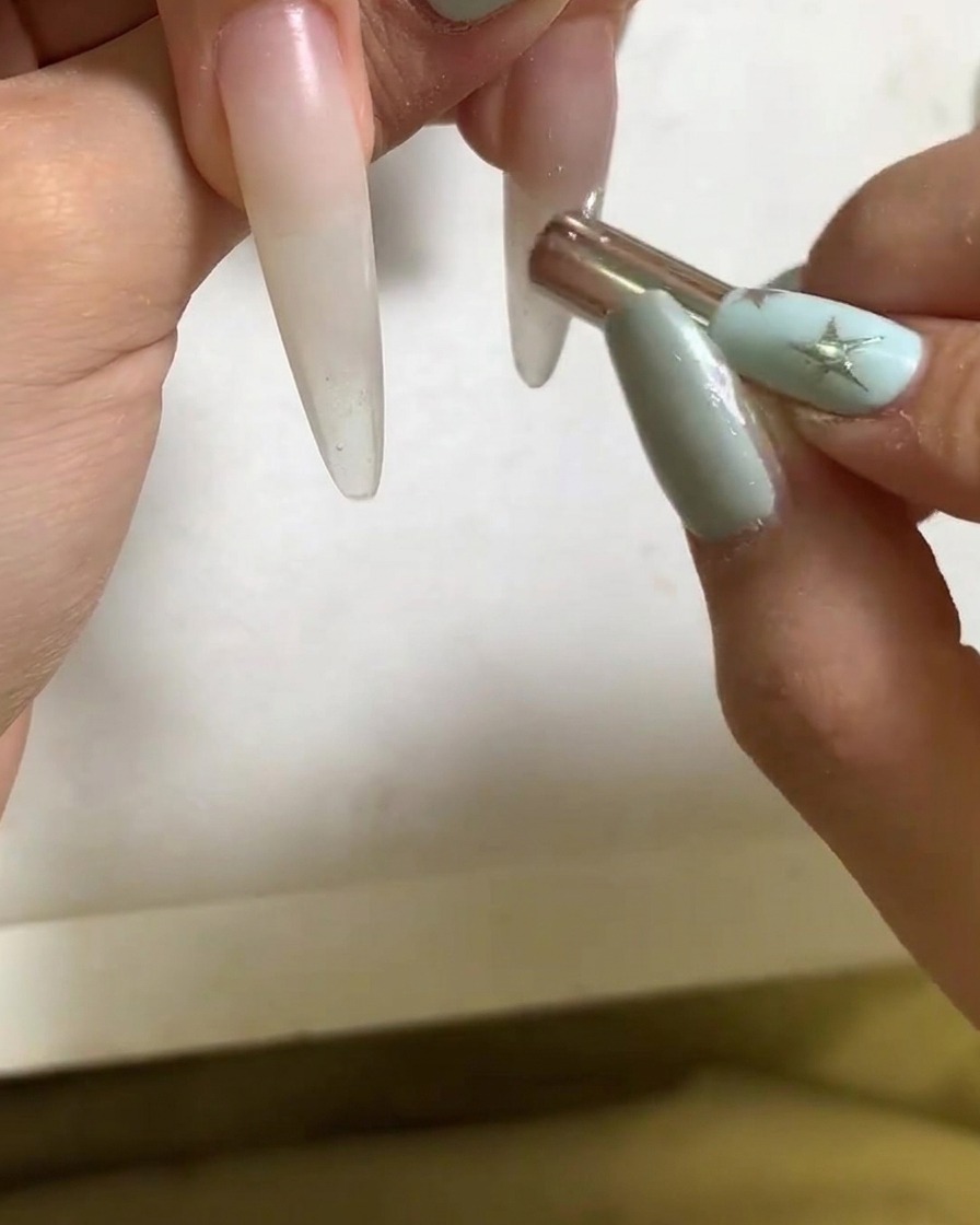 Ein kleiner Magnetstab formt die Lichtreflexion auf einem mit Gel beschichteten Fingernagel.