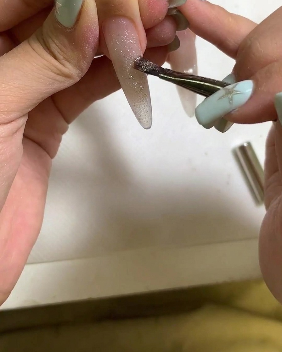 Ein Pinsel trägt Cat-Eye-Gel-Polish auf einen verlängerten Fingernagel auf.