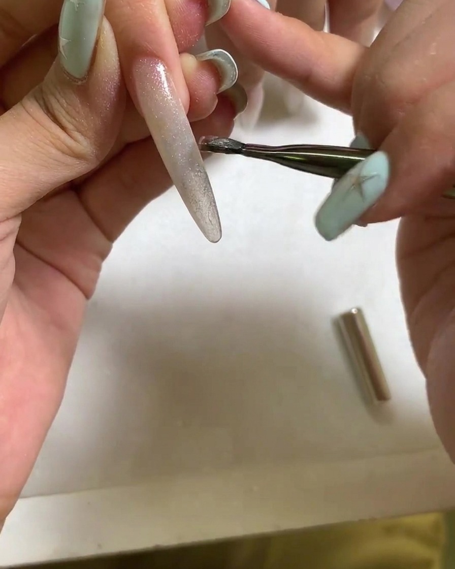 Ein Magnetwerkzeug wird in der Nähe der Oberfläche eines nassen Cat-Eye-Gelnagels gehalten, um eine helle, konzentrierte Lichtreflexion zu bilden.