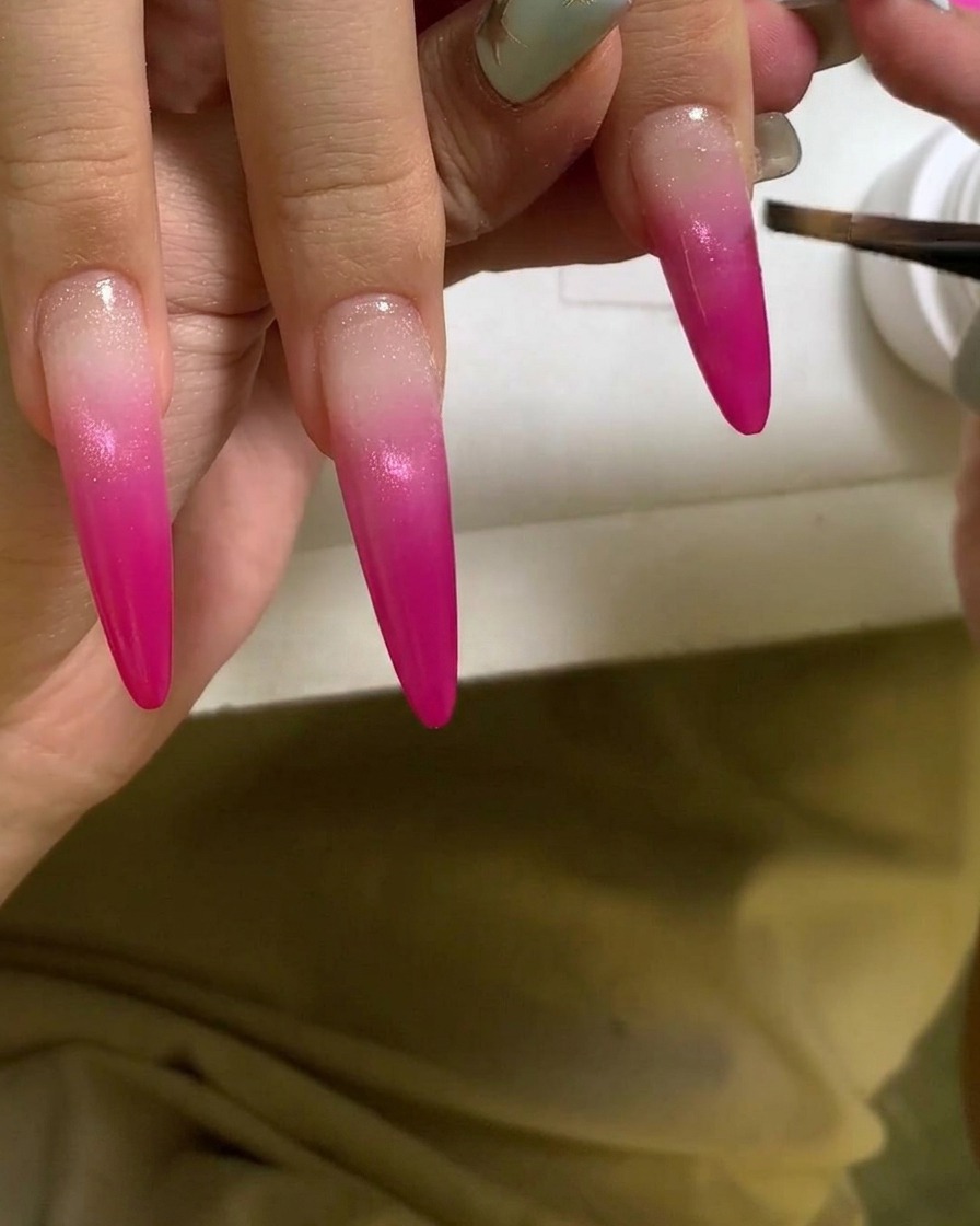 Ein Pinsel trägt eine klare, glänzende Gelschicht über einen lebendigen pinken Verlaufnagel auf.