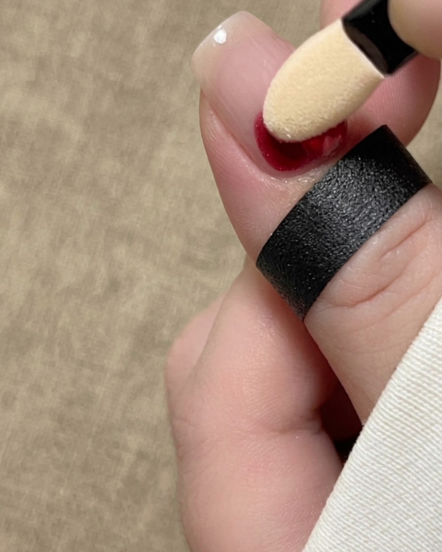 Ein Lidschatten-Schwammapplikator tupft rotes Tintenpigment an die Basis eines Fingernagels.