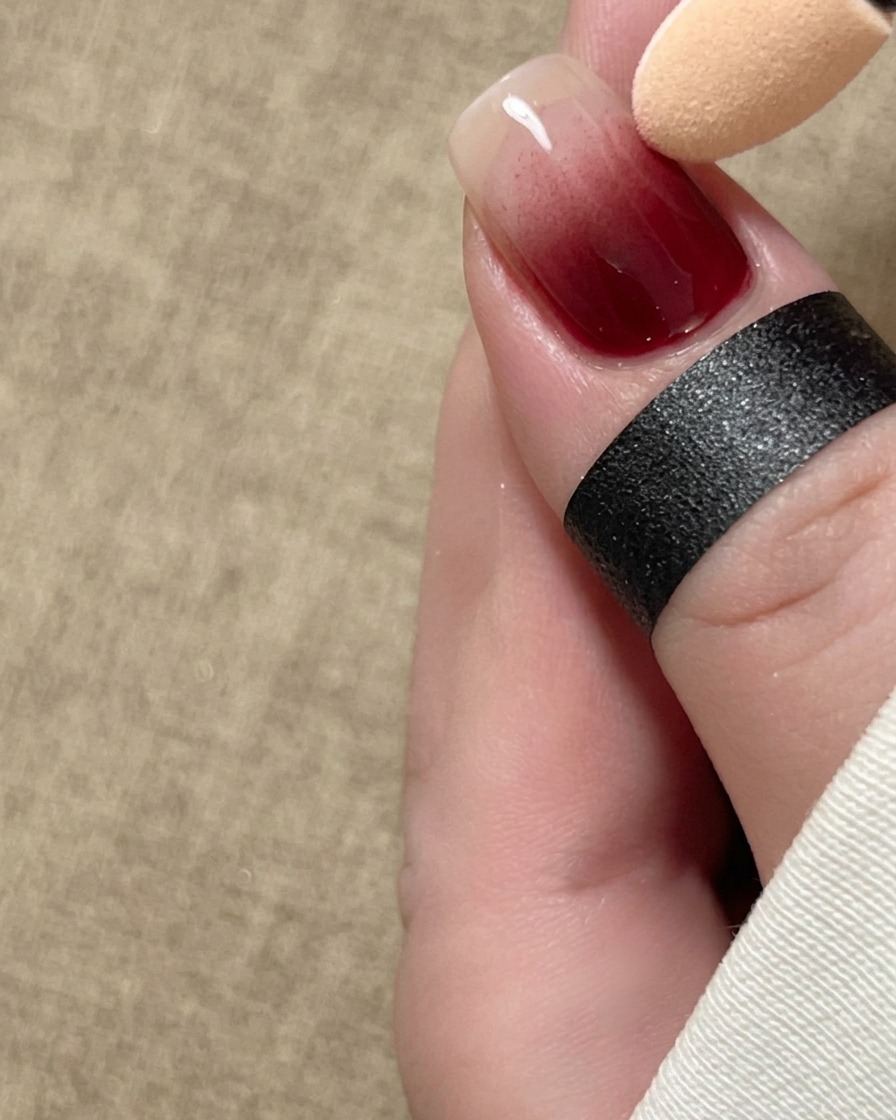 Ein Schwammapplikator verblendet sanft rotes Pigment in einem Ombré-Verlauf über die Länge eines Fingernagels.