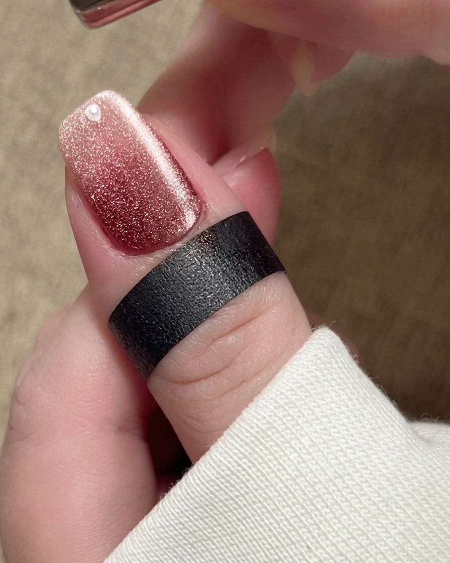 Ein Magnet wird nahe an den Nagel gehalten, wodurch die magnetischen Partikel im beigen Lack zu einem hellen, breiten Schimmerband verschoben werden.