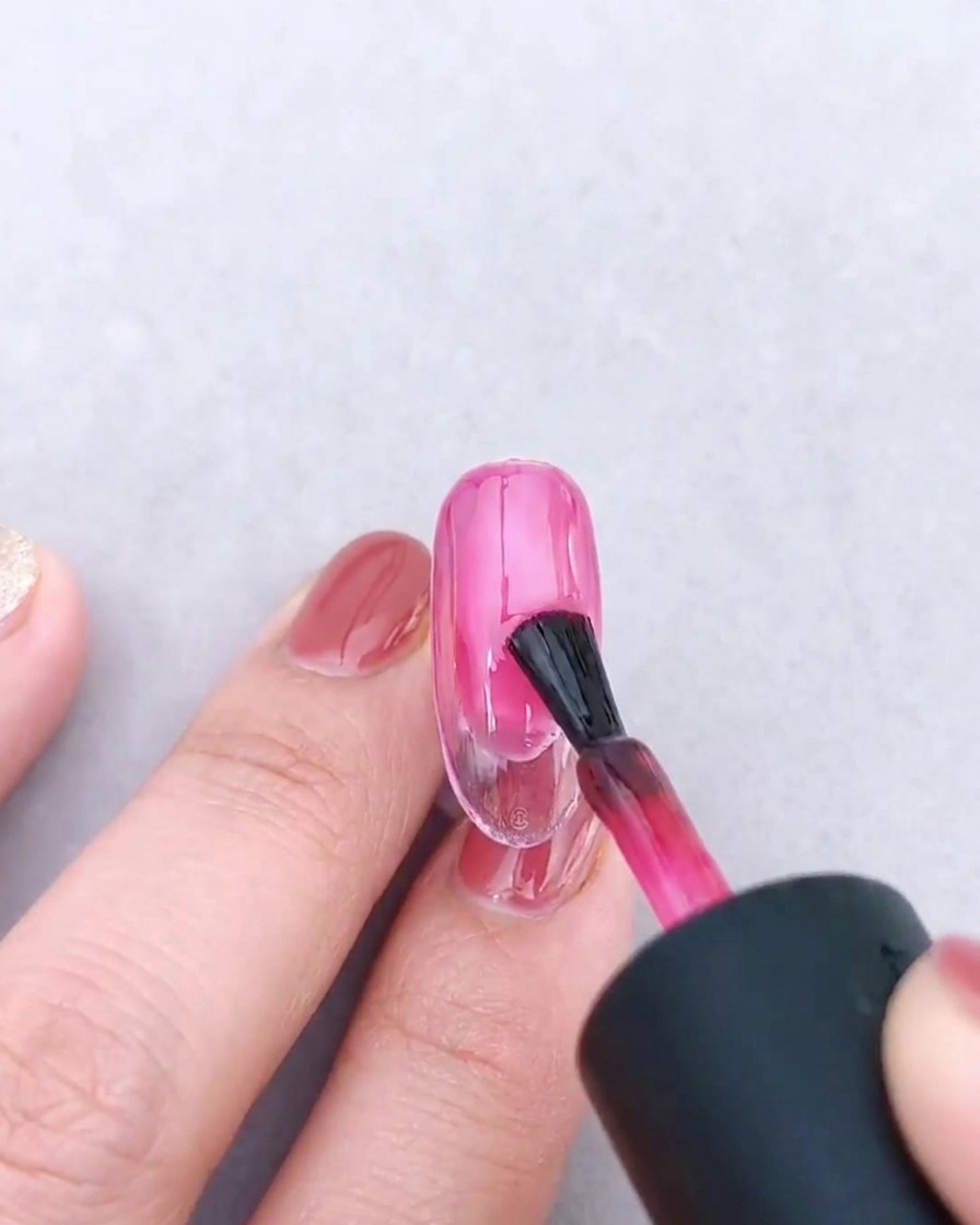 Eine Nagellackbürste trägt eine zweite Schicht transluzentes rosa Gel über den bestehenden Farbverlauf auf.