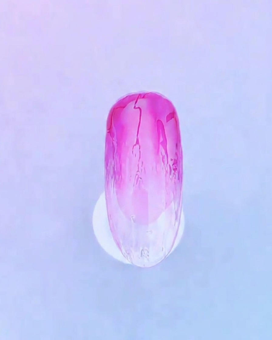 Nahaufnahme einer Nagellackbürste, die eine klare, gleichmäßige Schicht Base Gel über das bestehende rosa Ombré-Nageldesign aufträgt.