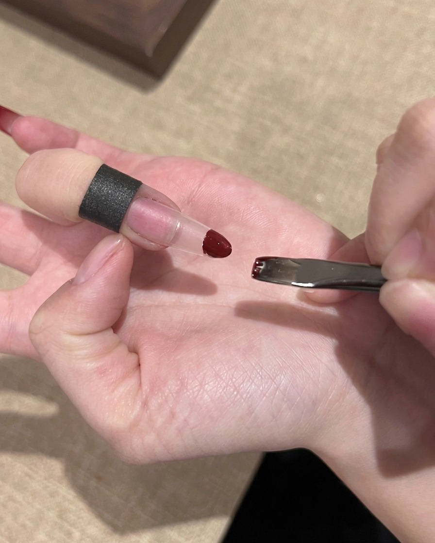 Eine Hand, die einen kleinen Schwamm verwendet, um rotes Gel-Polish auf die Spitze einer künstlichen Nagelverlängerung zu tupfen.