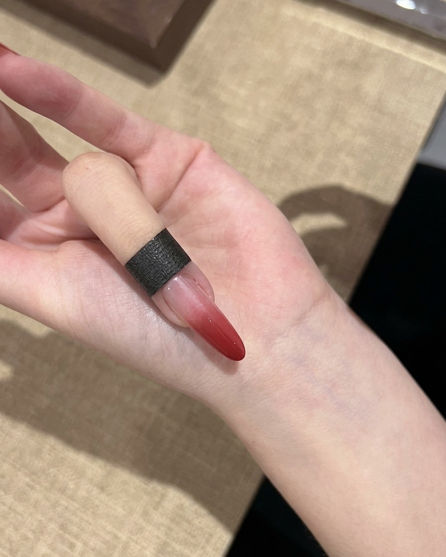 Ein einzelner Fingernagel zeigt einen ausgehärteten roten Farbverlauf, der von Dunkelrot zu klar übergeht.