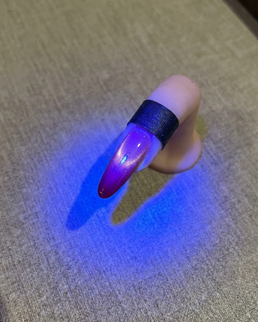 Ein Nagel unter einer blauen UV-Lampe, der ein glänzendes Cat-Eye-Finish zeigt.