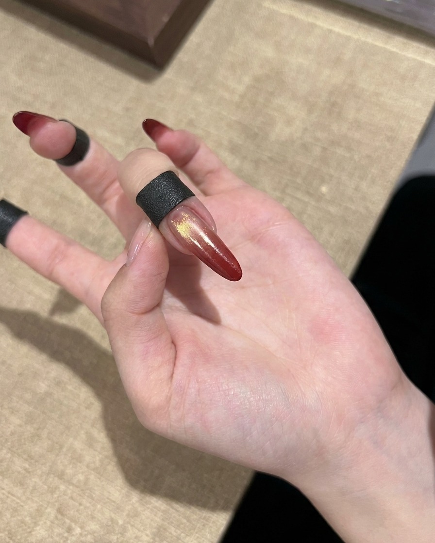Ein fertiger roter Cat-Eye-Farbverlaufsnagel mit goldenen Akzenten auf einer Hand.