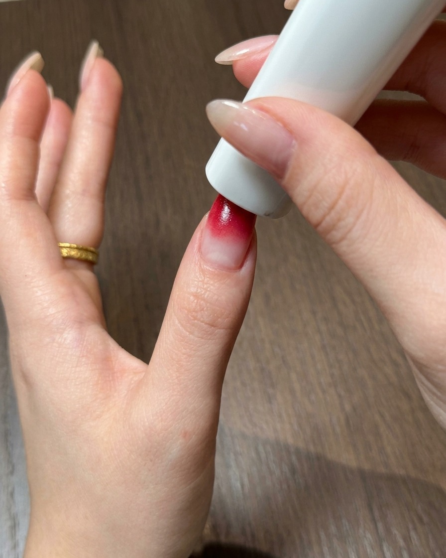 Ein Daumen, der sich direkt unter einer tragbaren weißen UV- und LED-Nagellampe befindet, um das rote Ombré-Gel auszuhärten.