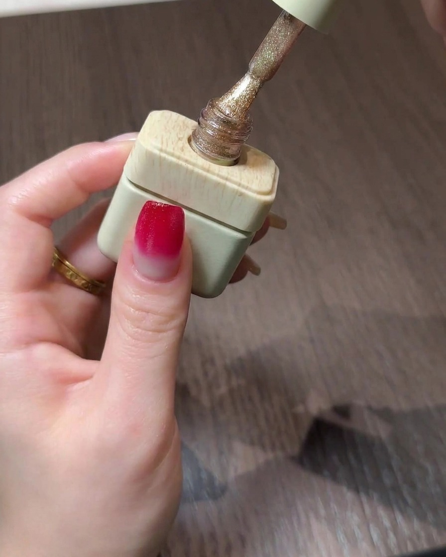 Eine Flasche goldenes Cat-Eye-Gel-Polish mit dem Pinsel über einem Verlaufsnagel.