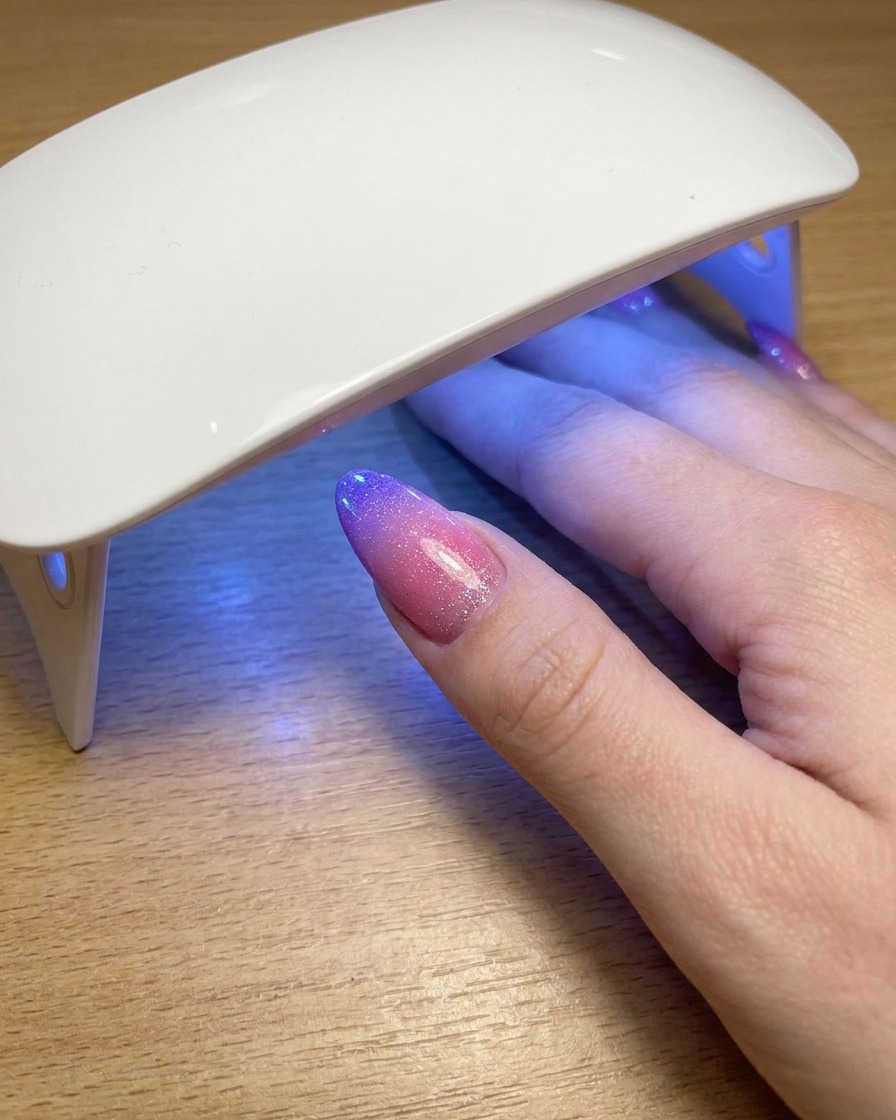 Ein Daumen, der unter einer tragbaren UV-Lampe ruht, während die letzte Schicht Cat-Eye-Gel-Polish aushärtet.