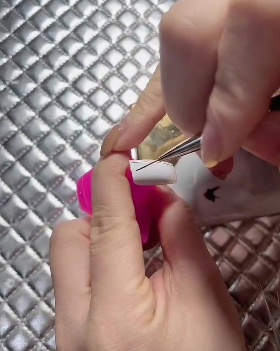 Eine Nahaufnahme einer Nageldesignerin, die Gitterlinien über eine weiße Nagelplatte erweitert.