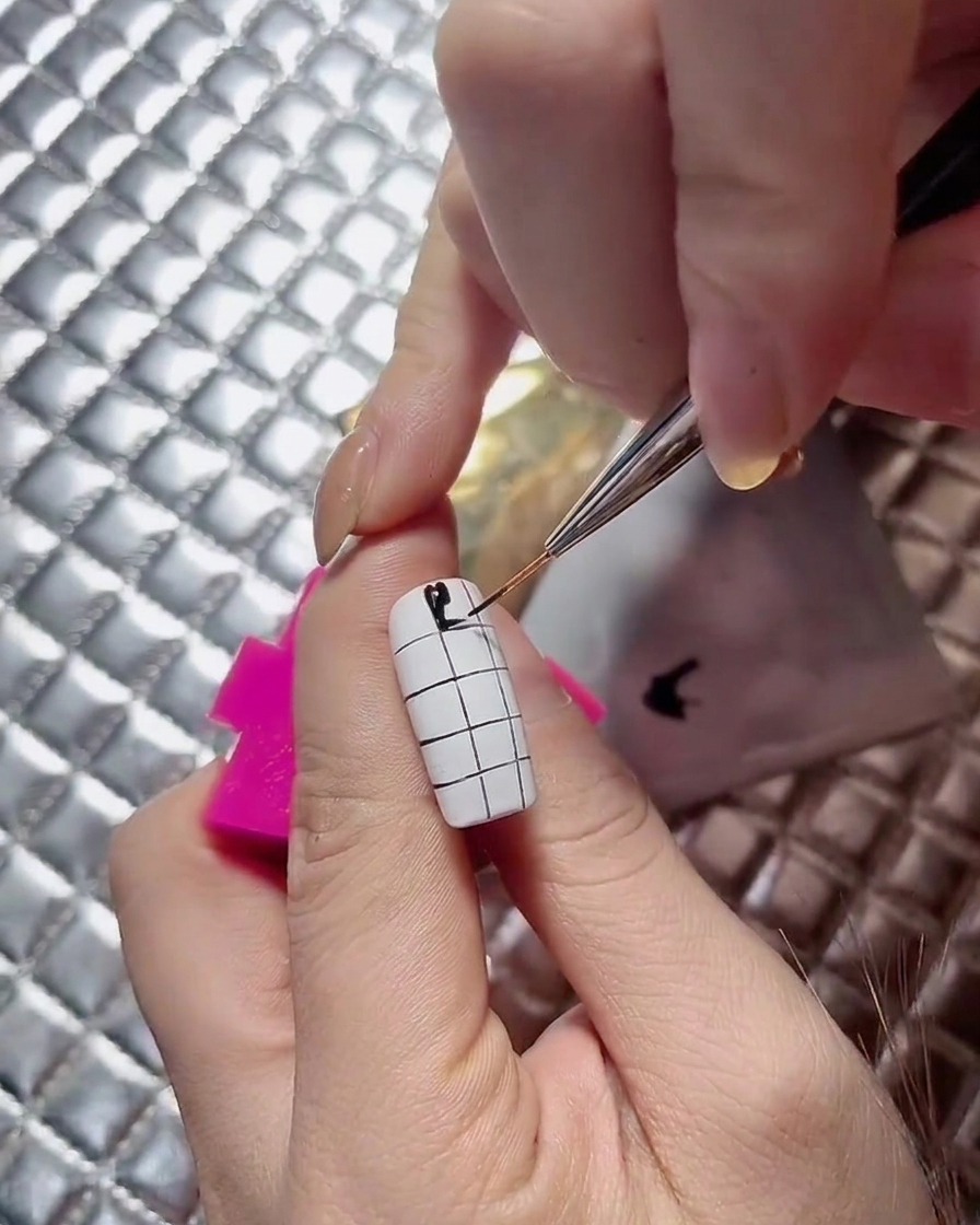 Eine Nageldesignerin führt die abwechselnden schwarzen Quadrate auf einem Schachbrett-Nageldesign fort.