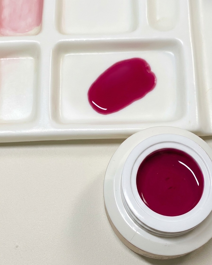 Eine Mischpalette zeigt einen Tropfen dunkelrosa Gelpolitur neben einem geöffneten Tiegel mit drachenfrucht-rotem Gel.