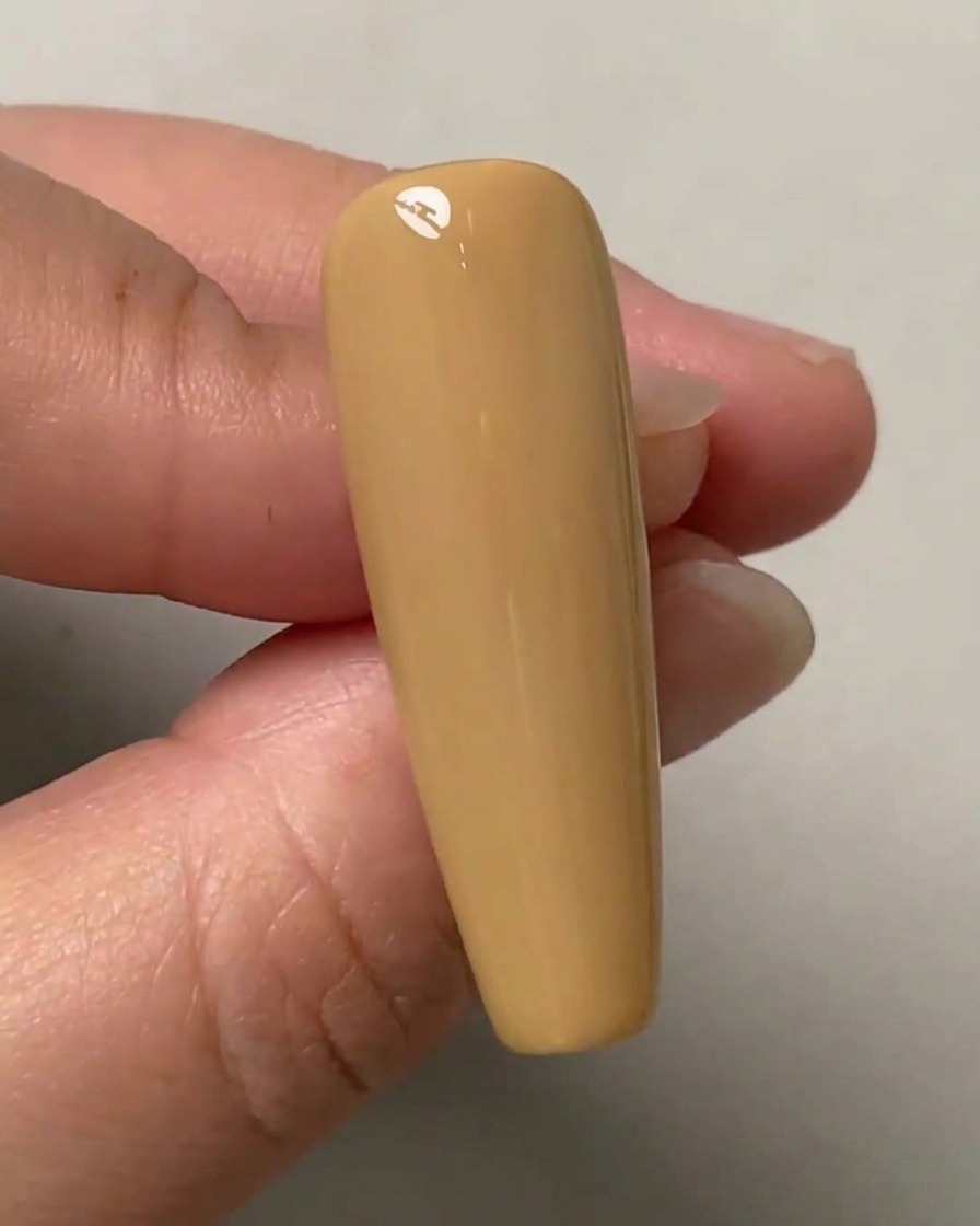 Eine Hand hält einen nudefarbenen Testnagel mit drei schwachen Punkten, die vertikal in der Mitte markiert sind.