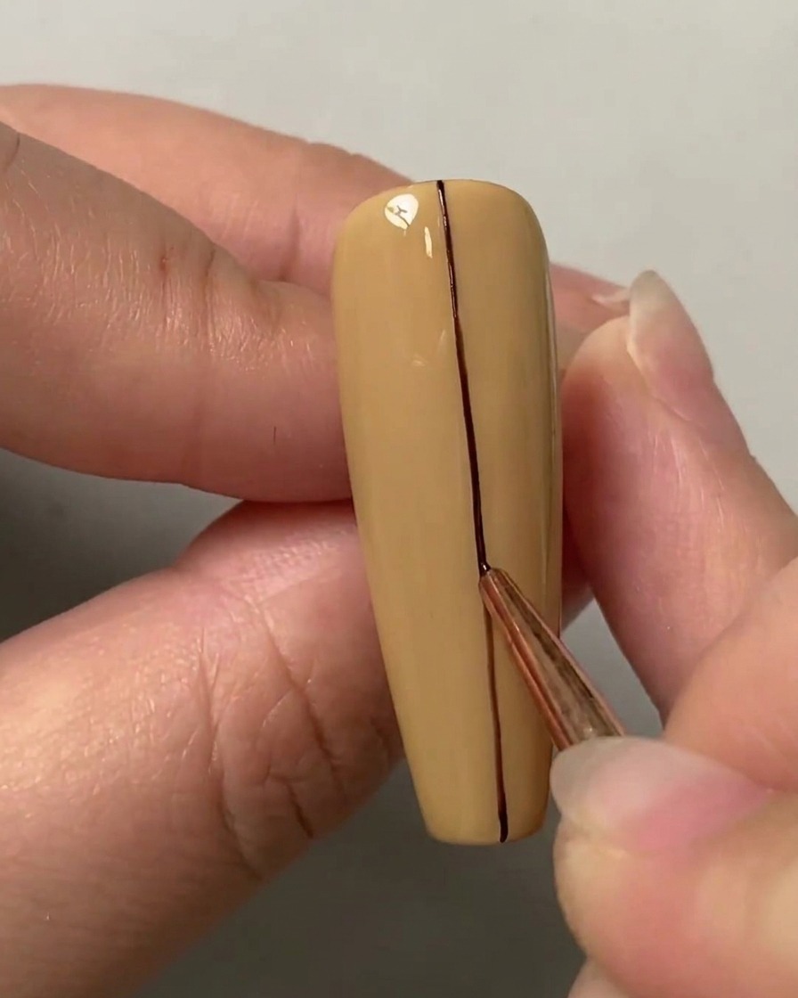 Ein Liner-Pinsel zieht eine gerade dunkle Linie die vertikale Mitte eines nudefarbenen Nagels hinunter.