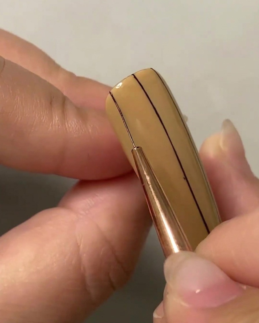 Ein Liner-Pinsel zeichnet eine zweite parallele vertikale Linie auf der linken Seite des Nagels.