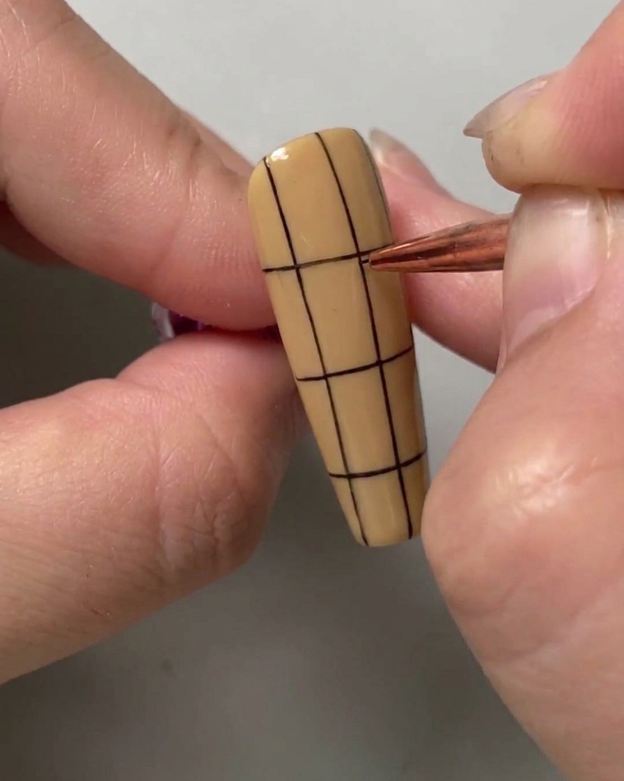 Ein Nail-Art-Pinsel zieht eine horizontale schwarze Linie über die obere Hälfte eines vertikal gestreiften Nagels.
