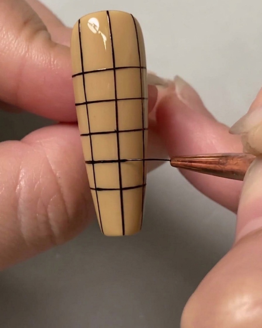 Ein Nail-Art-Pinsel zieht die letzten horizontalen Linien, um ein kleines, gleichmäßiges Quadratgitter über den gesamten Nagel zu vervollständigen.