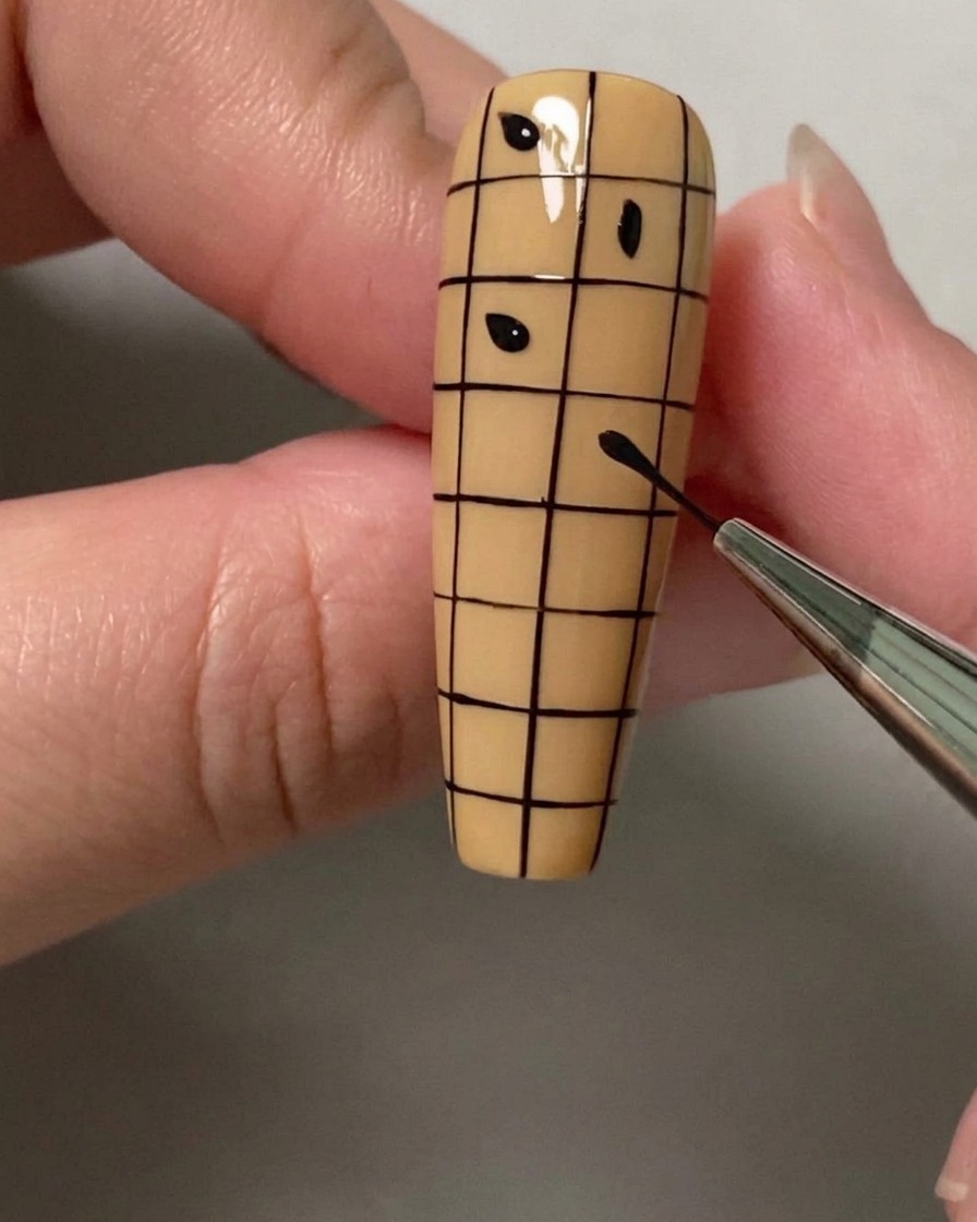 Ein Dotting-Tool oder Pinsel platziert kleine schwarze Punkte in abwechselnden Quadraten eines Gitters auf einem Nagel.