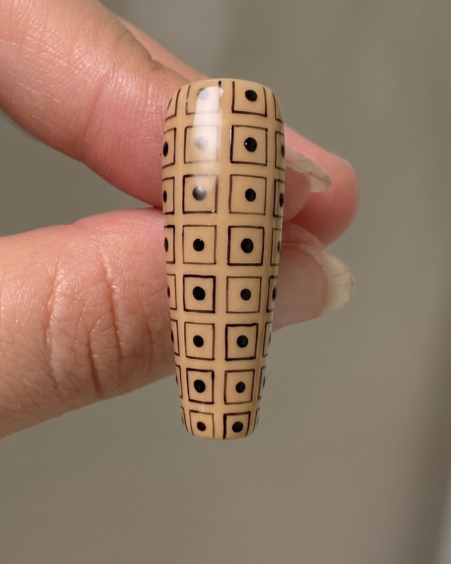 Ein langer Nude-Nagel mit einem handgezeichneten schwarzen Gitter, das abwechselnde schwarze Punkte in den Quadraten aufweist.