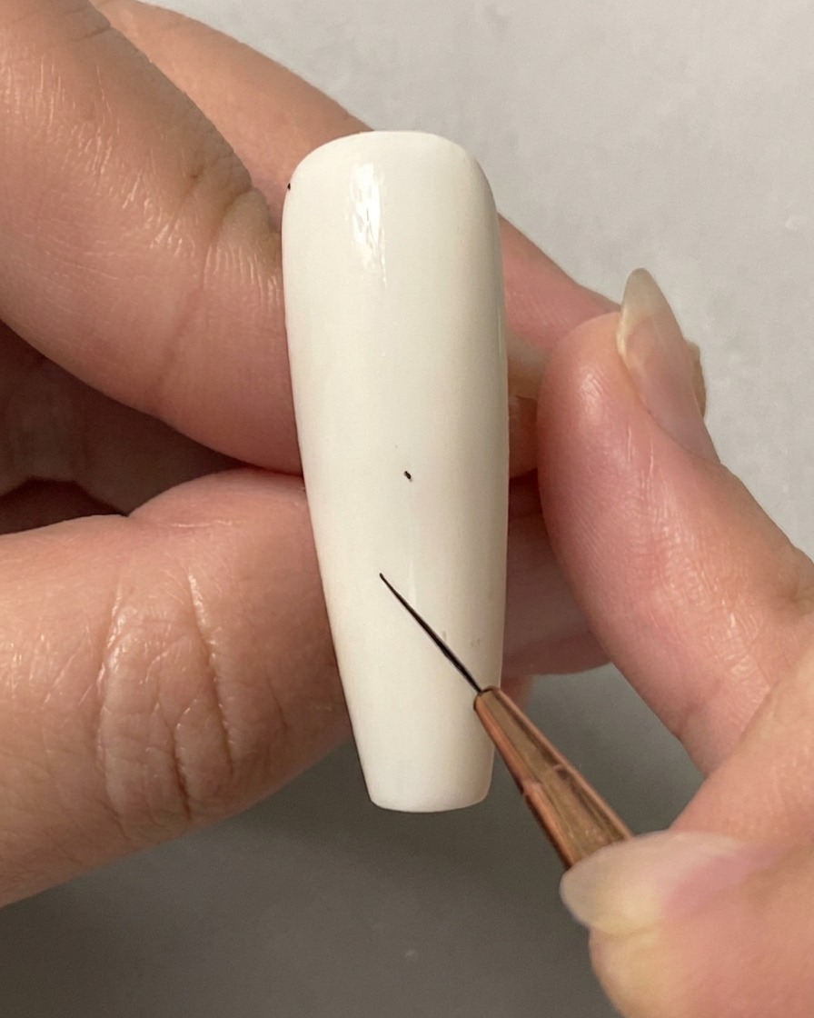 Eine Hand verwendet einen feinen Liner-Pinsel, um einen winzigen Punkt auf einem einfarbigen weißen Nagel zu platzieren.