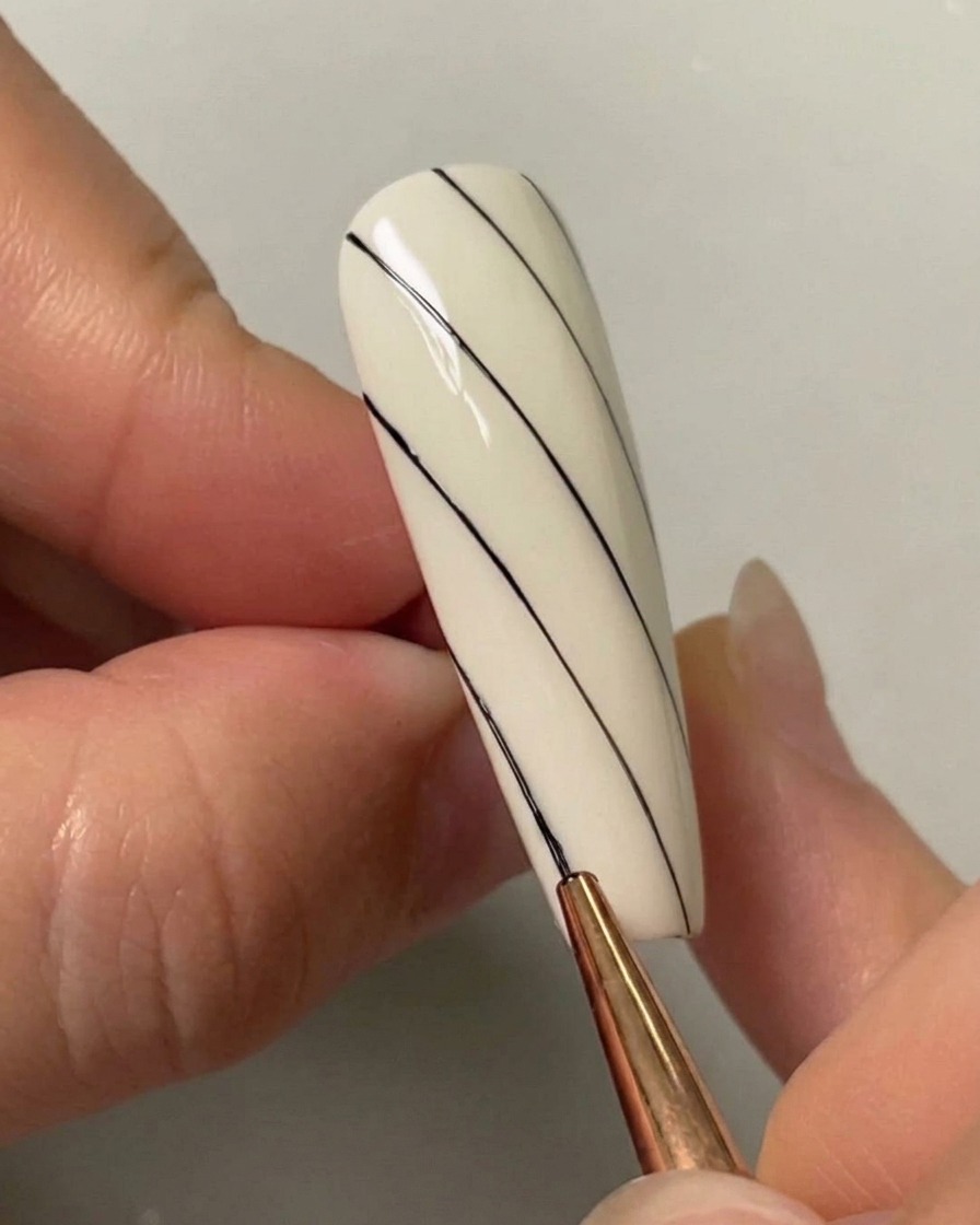 Ein Nail-Art-Pinsel zieht eine dritte diagonale schwarze Linie auf der unteren linken Seite eines bemalten weißen Nagels.