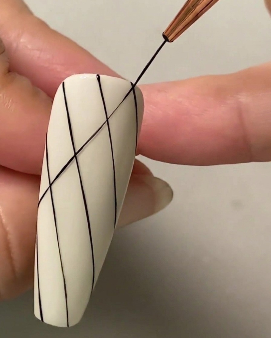 Ein feiner Liner-Pinsel zieht eine sich kreuzende diagonale schwarze Linie über bestehende parallele Linien, um ein Rautengittermuster zu bilden.