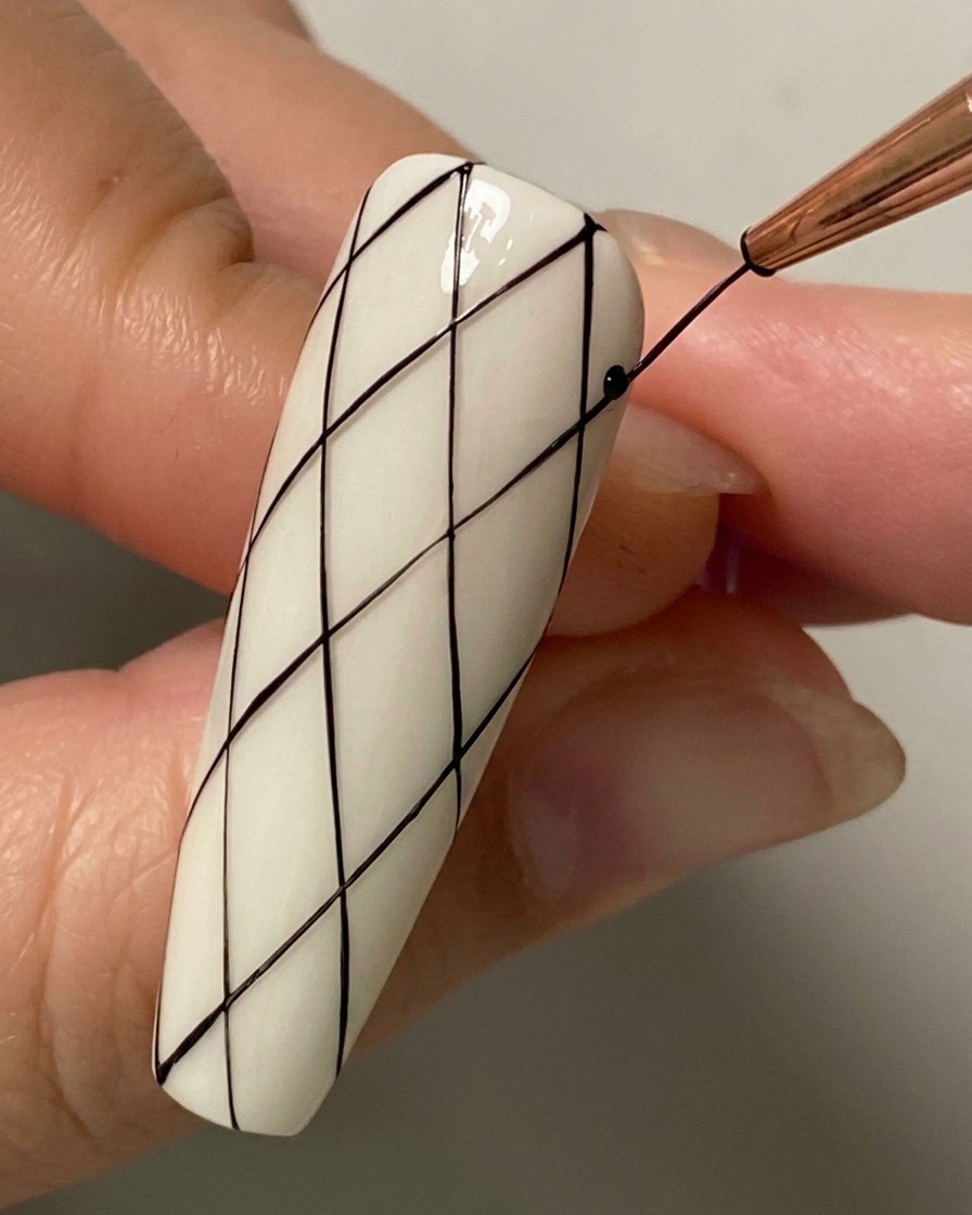 Eine Nahaufnahme eines Liner-Pinsels, der eine diagonale Schnittlinie in der unteren Hälfte des Nagels zieht.