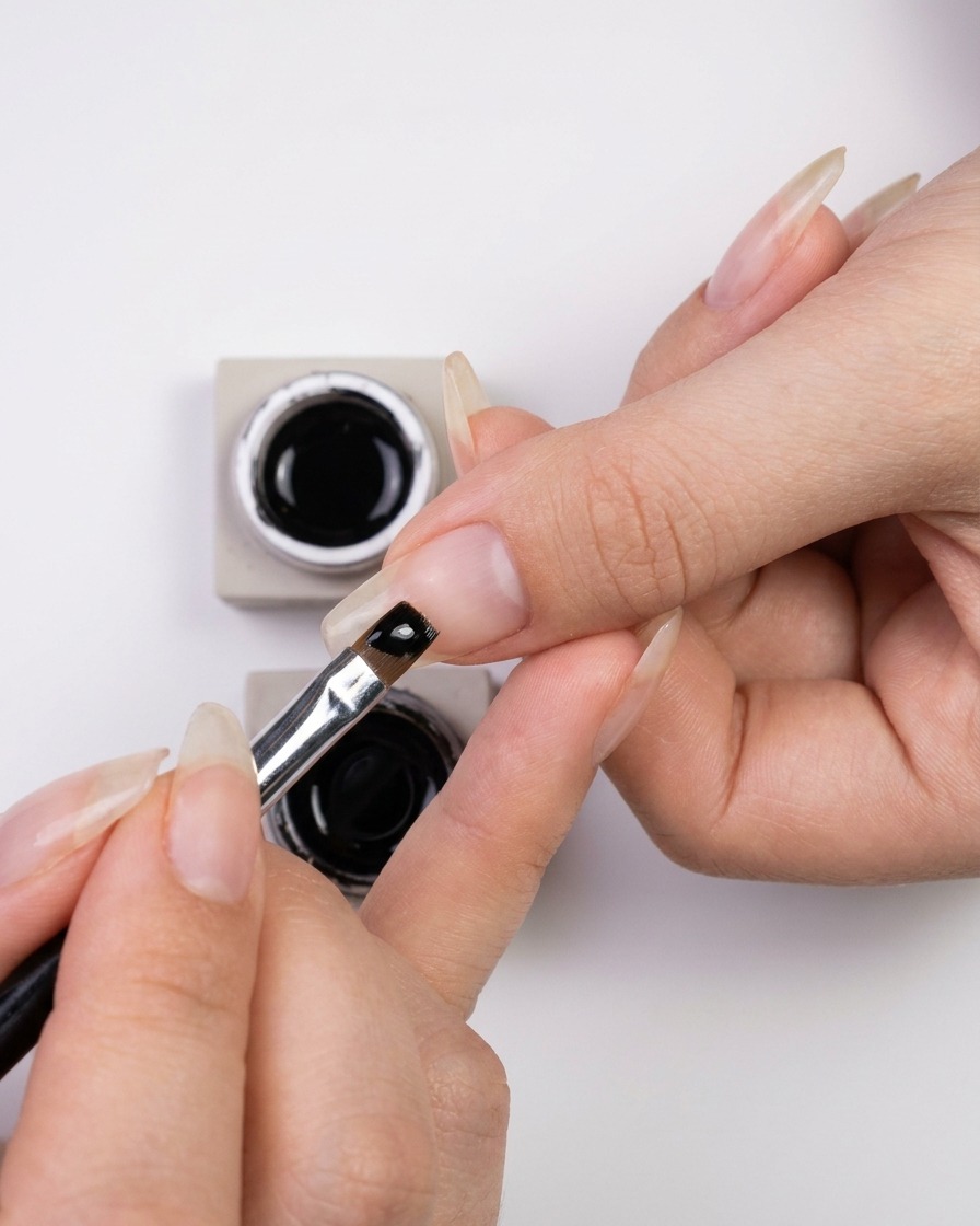 Eine Hand taucht einen feinen Nailart-Liner-Pinsel in ein kleines Gefäß mit glänzendem schwarzen Gel-Nagellack.