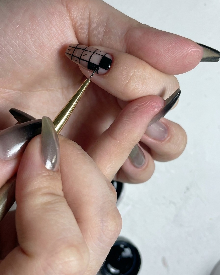 Ein feiner Pinsel korrigiert die Ränder der ausgefüllten schwarzen Quadrate in einem Karo-Nailart-Design, um sie scharf zu machen.