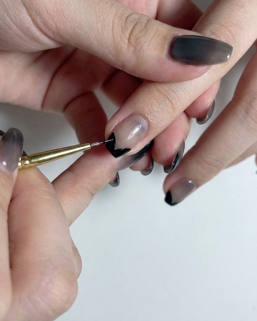 Ein feiner Liner-Pinsel zieht eine gerade vertikale schwarze Linie die Mitte eines rauchig durchscheinenden Gradient-Nagels hinunter.