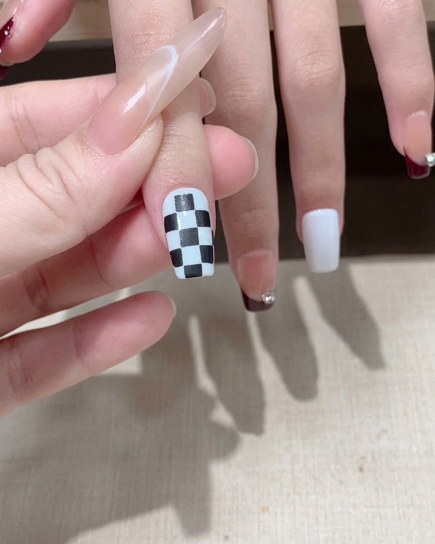 Ein Pinsel trägt einen glänzenden Top Coat über einem fertigen schwarz-weißen Schachbrett-Nageldesign auf.