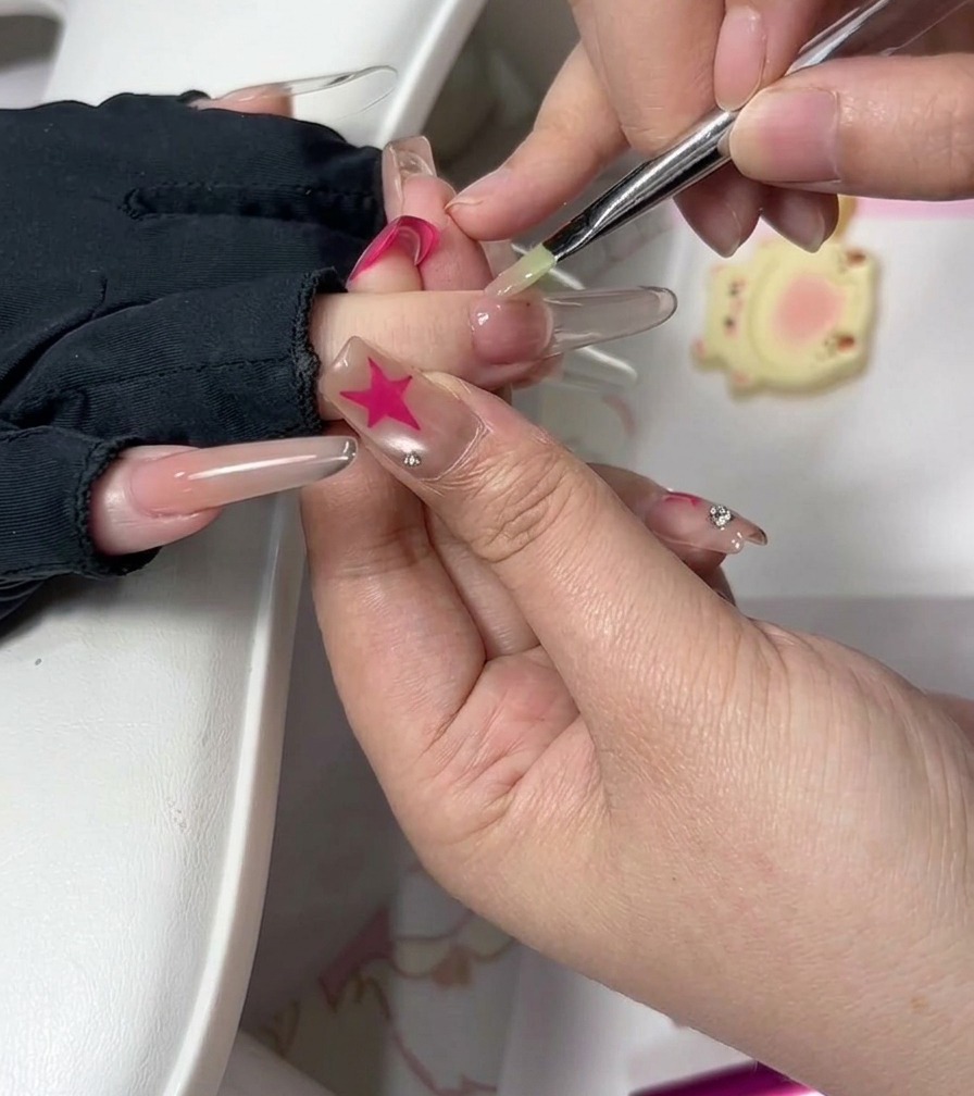 Eine Nageldesignerin verwendet einen feinen Pinsel, um das Gel in der Nähe der Nagelhaut auf einem verlängerten Nagel sorgfältig zu glätten.