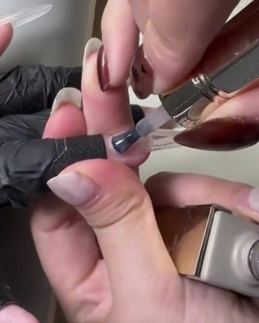 Nahaufnahme eines Pinsels, der hellrosafarbenes, transparentes Gel über die Nagelverlängerung streicht.