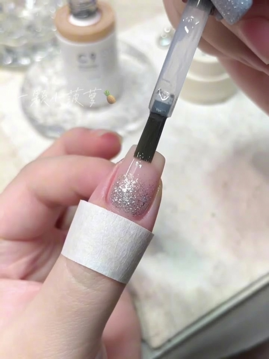 Ein Flaschenpinsel trägt einen klaren Top Coat über einen Nagel mit Crushed-Diamond-Glitzer auf.