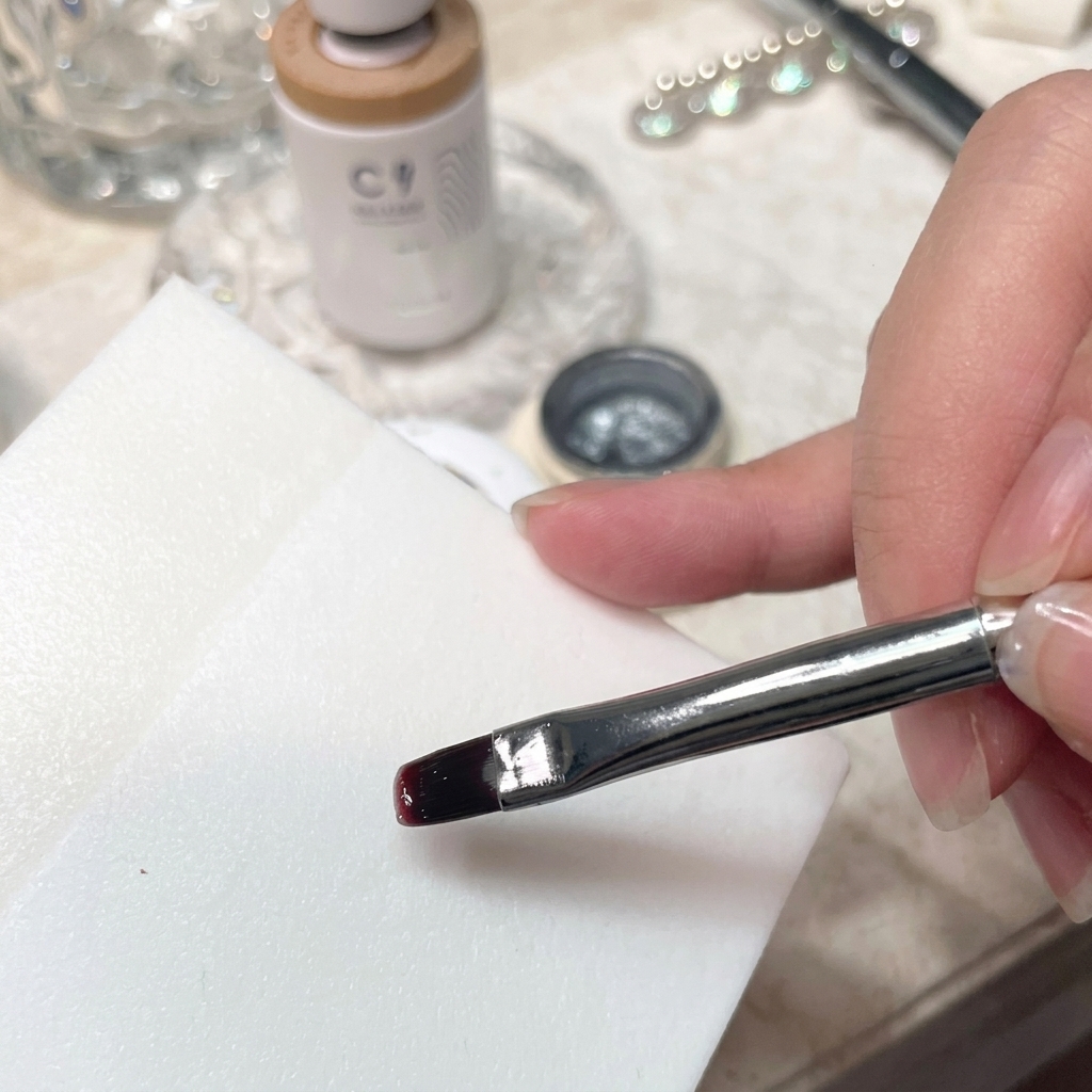 Eine detaillierte Nahaufnahme eines Pinsels, der Gel-Nagellack auf einer glatten weißen Palettenoberfläche mischt.