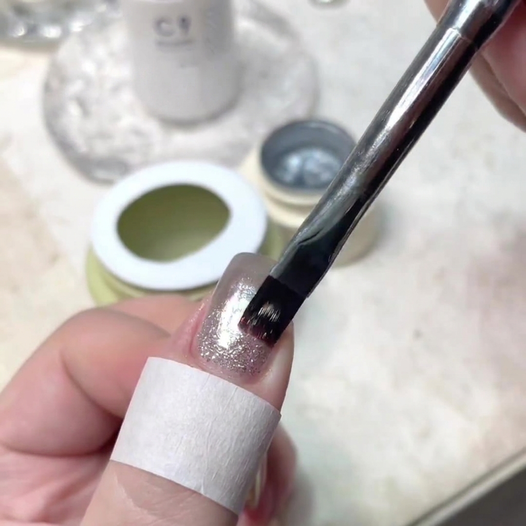Ein Nagelpinsel trägt präzise einen dünnen Strich schimmernden Gels auf die Mitte eines manikürten Nagels auf.
