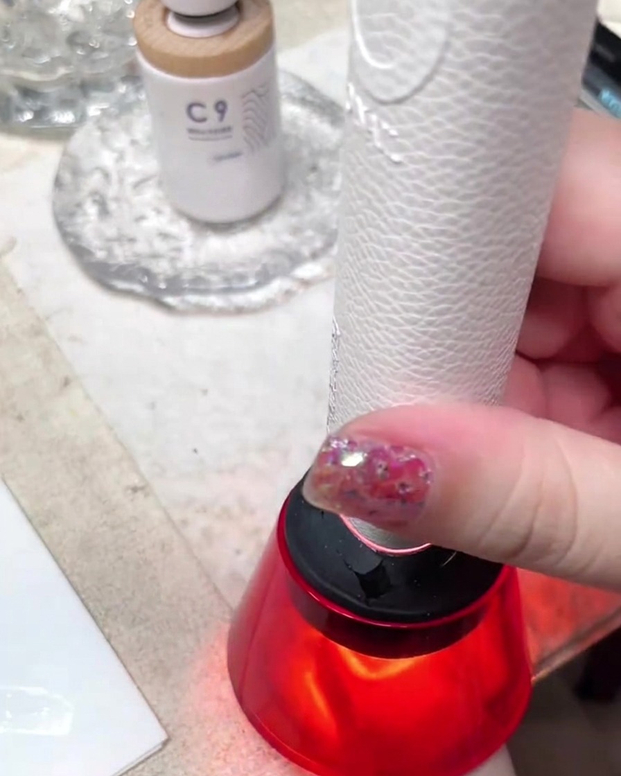 Eine kompakte tragbare rote Mini-UV-/LED-Lampe härtet ein Nageldesign in einem gut beleuchteten Studio-Arbeitsbereich aus.