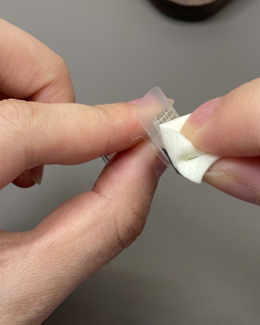 Ein Make-up-Schwämmchen tupft off-white Gel-Nagellack auf einen French Hilfsaufkleber auf einem Nagel.
