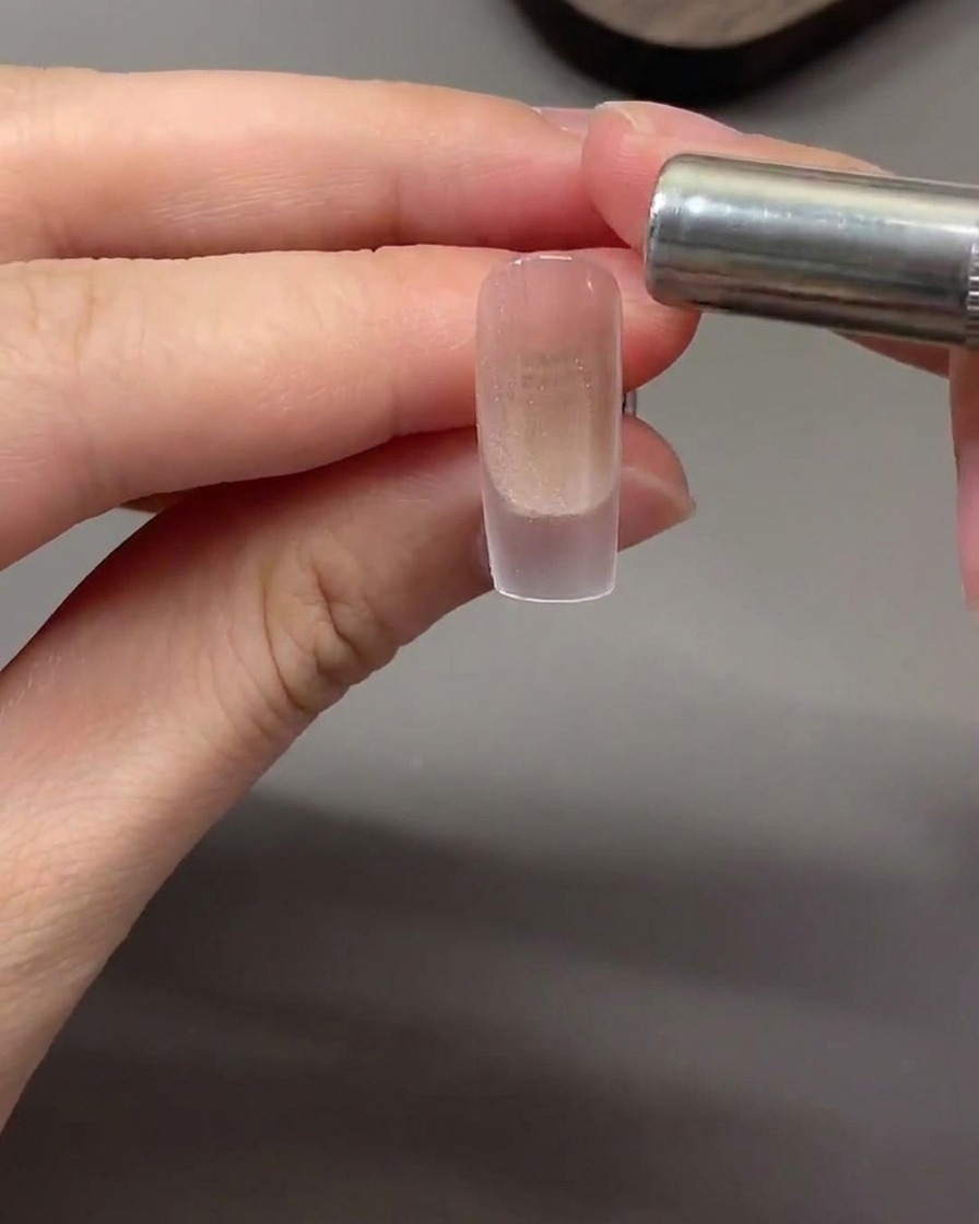 Ein zylindrischer Magnet wird waagerecht nahe der Nagelspitze gehalten, um magnetische Cat-Eye-Partikel zu einem Lichtband zu ziehen.
