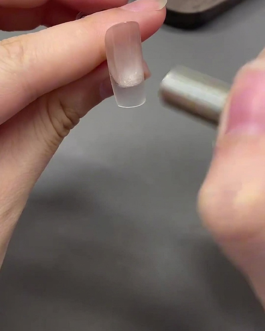 Ein Magnet bewegt sich in einer geschwungenen Bewegung um die Nagelspitze, um das Cat-Eye-Gel in einen Glasperlen-Effekt zu formen.