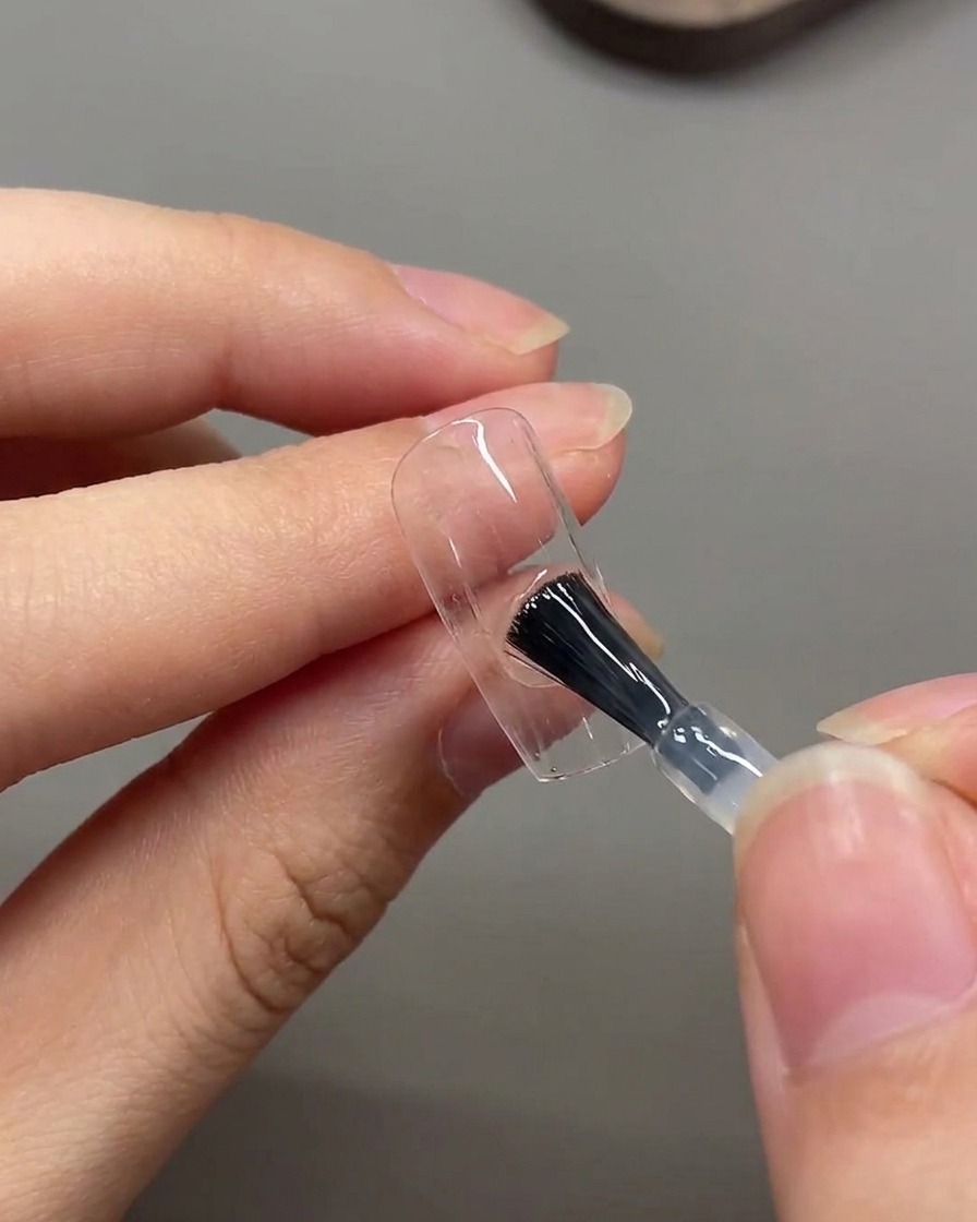 Ein Pinsel trägt eine Schicht matten Top Coat über die gesamte Oberfläche des Nagels auf.