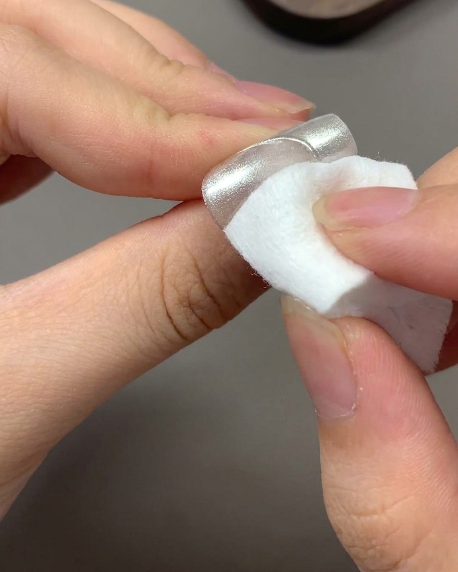 Ein sauberes, trockenes Tuch entfernt überschüssiges, herumschwebendes Chrom-Puder von einem Nagel.