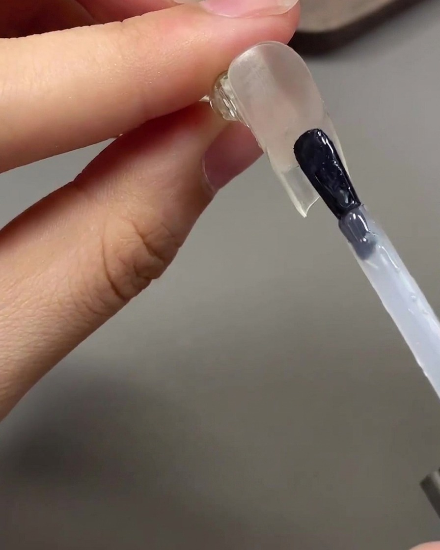 Ein Pinsel trägt klaren glänzenden Top Coat unter der verlängerten Nagelspitze auf.
