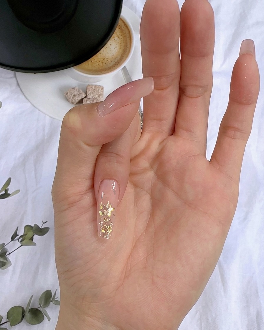 Eine Nahaufnahme von Blattgoldflocken, die auf die feuchte Glitterschicht eines Fingernagels gedrückt werden.